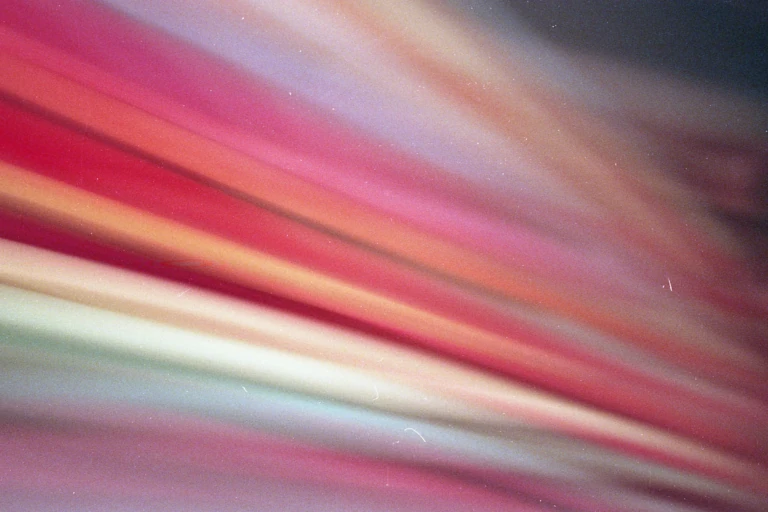 A blurred abstract image featuring streaks of various colors, including shades of red, pink, orange, and green.